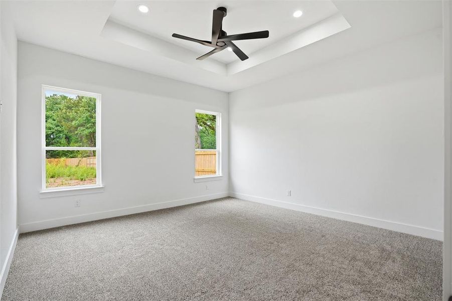 Spacious room featuring a tray ceiling with recessed lighting and a contemporary ceiling fan