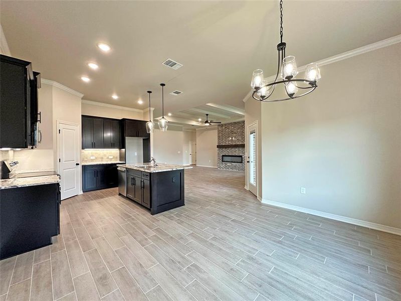 Kitchen with ornamental molding, dark cabinetry, light stone countertops, tasteful backsplash, and hanging light fixtures