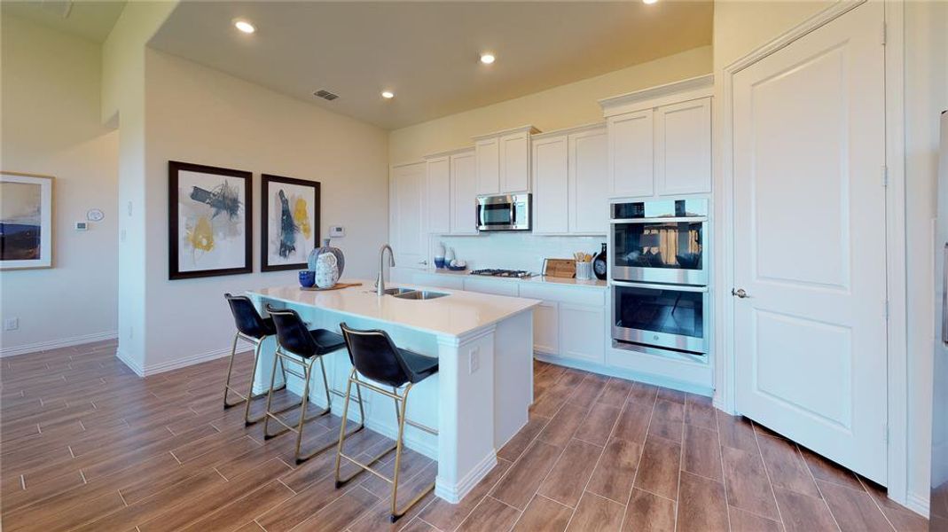 Kitchen featuring white cabinetry, a kitchen breakfast bar, stainless steel appliances, wood tiled floors, and a kitchen island with sink