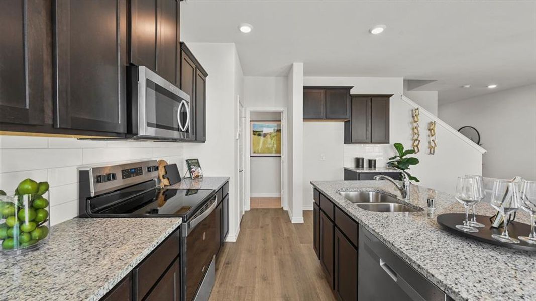 Kitchen with stainless steel appliances, backsplash, light stone countertops, dark wood-type flooring, and dark brown cabinets Kitchen with stainless steel appliances, backsplash, light stone countertops, dark wood-type flooring, and dark brown cabinets