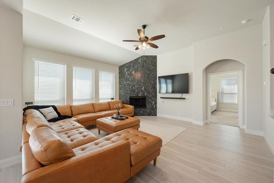 Living room with lofted ceiling, engineered flooring, a premium granite tiled fireplace, and neutral paint palette. Ceiling fan with light kit. All windows have cordless 2 inch blinds.