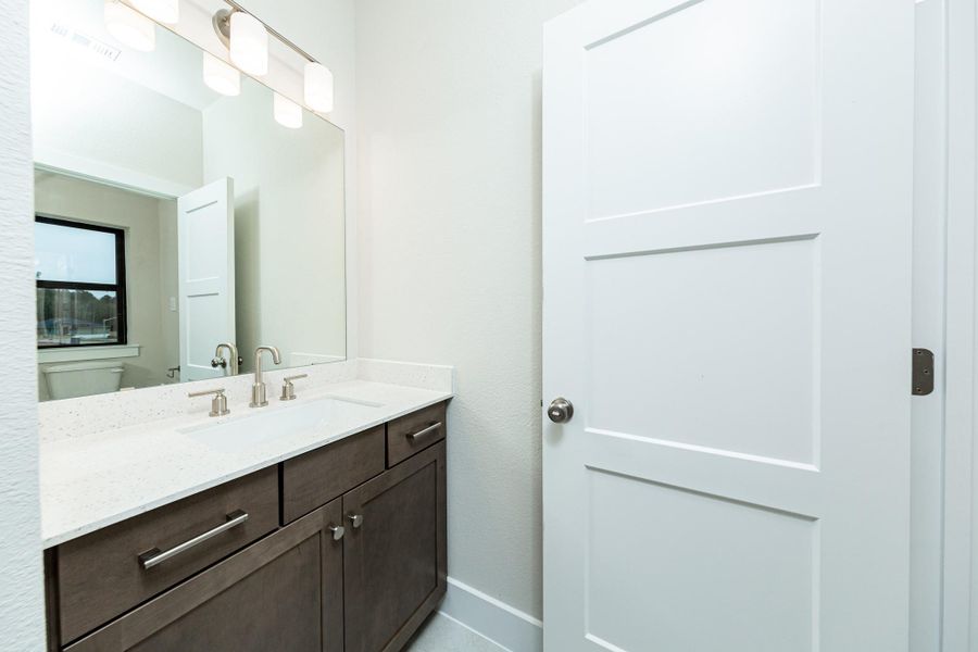 This well-appointed secondary bathroom offers exceptional functionality with stained cabinetry and white countertops. Sleek, brushed nickel fixtures and hardware as well as the chic light fixture complements this space. NOTE: Both secondary bedrooms have its own vanity and share the tub/shower combination and toilet.