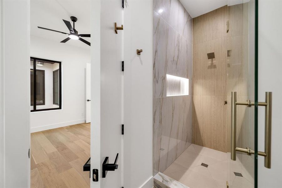 Walk-in shower featuring a glass enclosure with brass-finish hardware, tiled walls with an illuminated niche, and a contrasting tiled floor