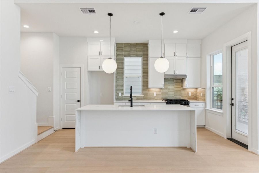 Large waterfall-edge island anchors the kitchen, offering generous workspace and seating. Matte black fixtures, quartz surfaces, and subtle tile accents lend a polished, modern aesthetic while maintaining a comfortable, inviting feel that connects seamlessly to the living area.