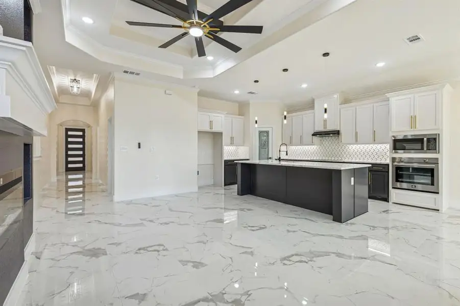 Kitchen with ornamental molding, two tone cabinetry, ceiling fan, decorative light fixtures, and stainless steel appliances