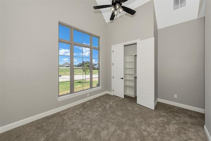Unfurnished bedroom with dark carpet, high vaulted ceiling, a ceiling fan, and a closet