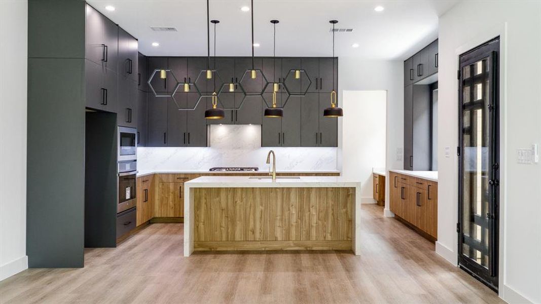 Kitchen featuring appliances with stainless steel finishes, sink, light hardwood / wood-style flooring, hanging light fixtures, and an island with sink