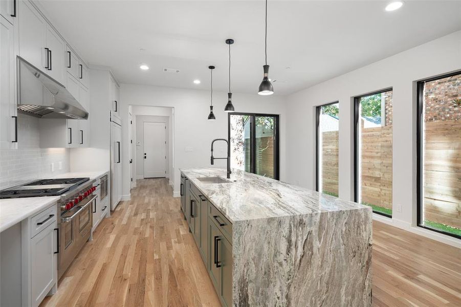 Kitchen featuring backsplash, light stone counters, a spacious island, pendant lighting, and white cabinets