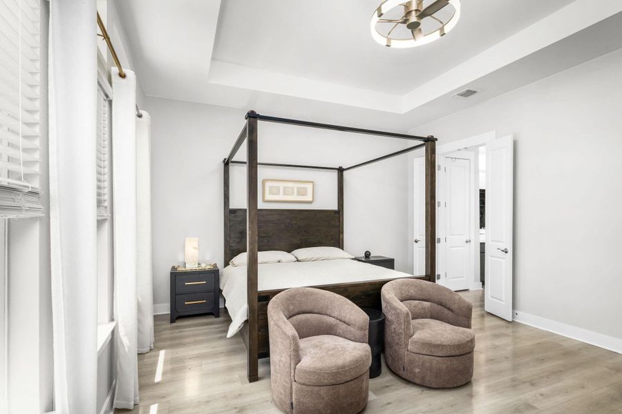 A grand canopy bed creates a serene focal point in this primary bedroom with light wood flooring and a sophisticated tray ceiling.