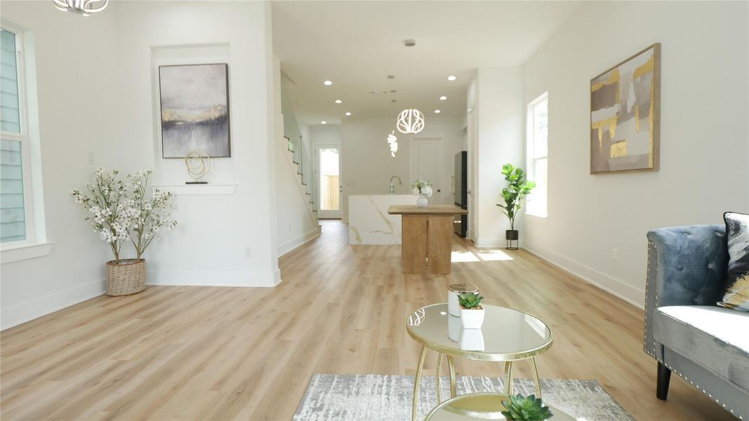 This photo showcases a bright, open-concept living space with modern decor. It features light wood flooring, a cozy seating area, and a view into the kitchen with stylish pendant lighting. Large windows allow natural light to illuminate the space, creating an inviting atmosphere. This photo showcases a bright, open-concept living space with modern decor. It features light wood flooring, a cozy seating area, and a view into the kitchen with stylish pendant lighting. Large windows allow natural light to illuminate the space, creating an inviting atmosphere.