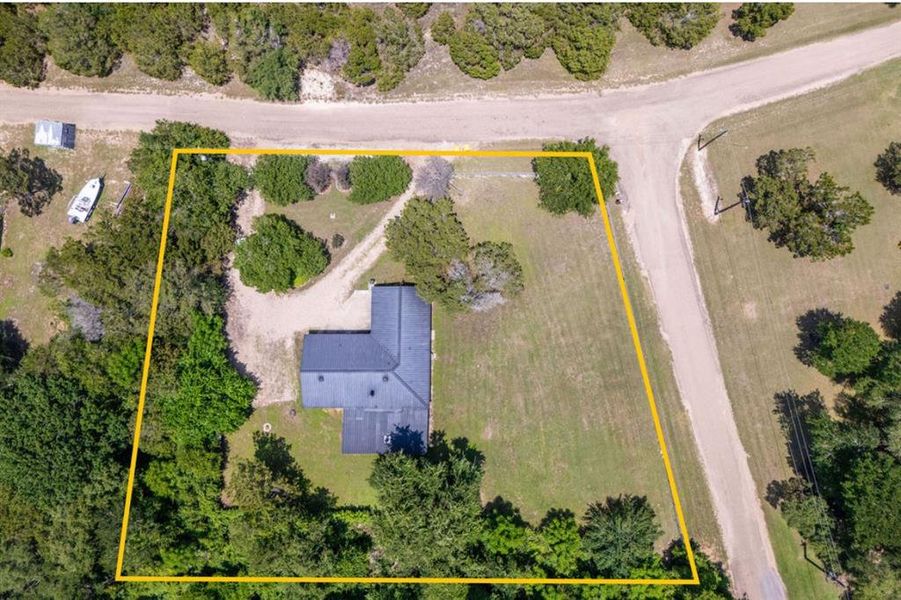 Aerial property outline featuring a dark-roofed structure, extensive green space, mature trees, and a gravel driveway