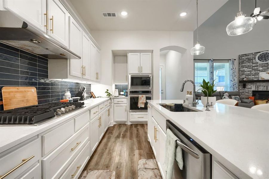 Kitchen with backsplash, sink, appliances with stainless steel finishes, decorative light fixtures, and white cabinetry