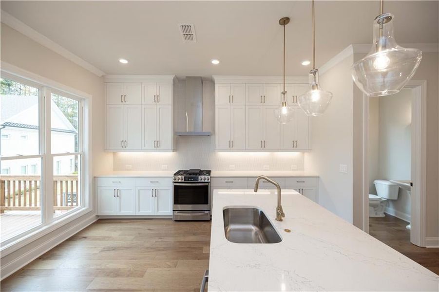 Kitchen featuring sink, stainless steel range with gas cooktop, pendant lighting, light stone countertops, and wall chimney range hood