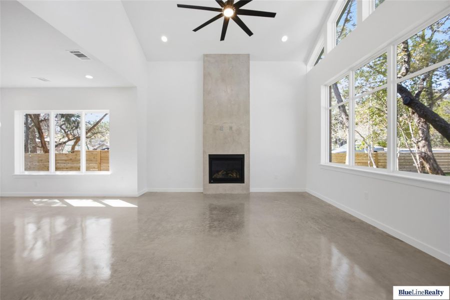 Unfurnished living room with concrete flooring, a ceiling fan, a large fireplace, a high ceiling, and recessed lighting