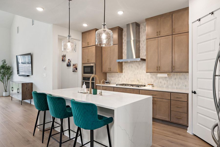 Bright kitchen with a waterfall countertop island, stainless steel appliances, wood-finish flooring, full-height cabinetry, and a sliding barn door
