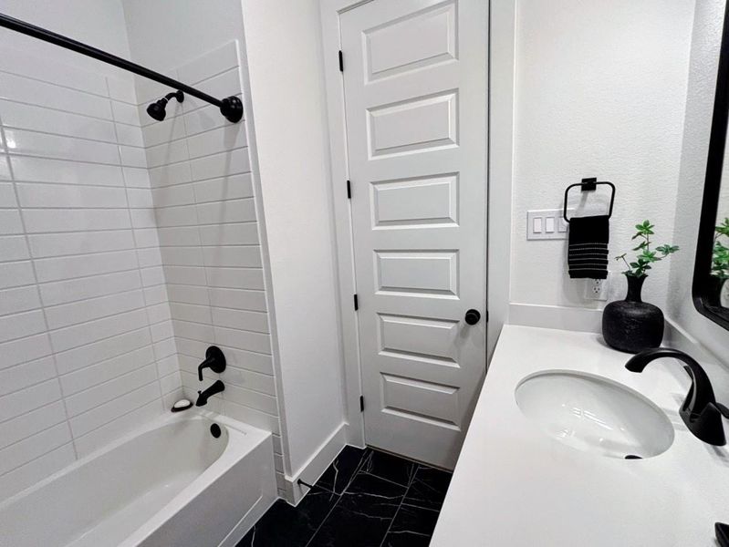 Modern bathroom #2 with a sleek design. Features a white tub-shower combo, black fixtures, and a stylish vanity with a round sink.