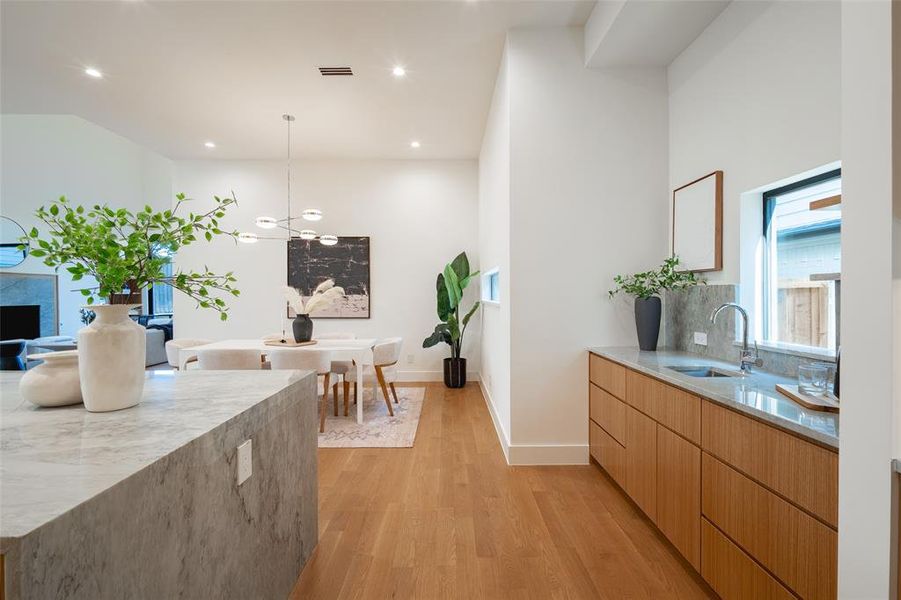 Kitchen featuring sink, a premium fireplace, tasteful backsplash, light hardwood / wood-style floors, and decorative light fixtures