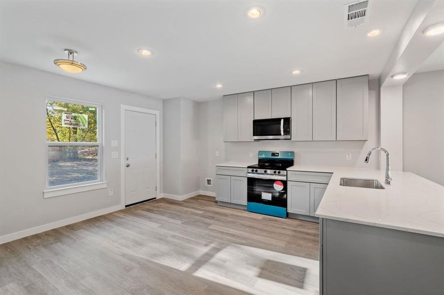 Kitchen featuring gray cabinetry, light stone counters, sink, and stove