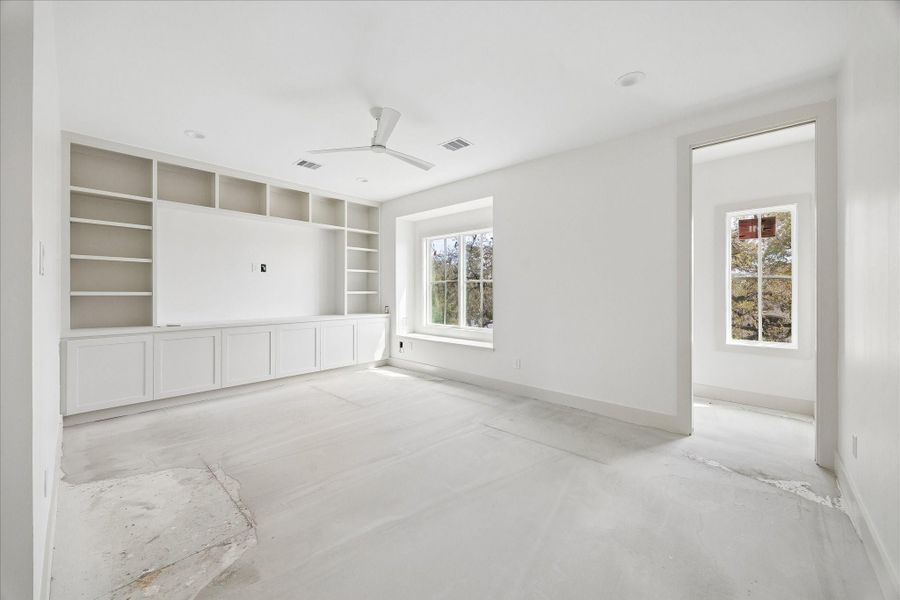 Versatile upstairs living space featuring custom built in cabinetry and shelving, ideal for a media room, game room, or secondary lounge. Large windows bring in abundant natural light while offering treetop views, creating a bright and inviting atmosphere. The open layout provides flexibility for a variety of uses, with seamless access to an adjacent room that could serve as a study, playroom, or additional workspace.