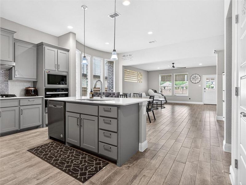 Open-concept kitchen featuring an island with built-in storage, white countertop, and stainless-steel sink Open-concept kitchen featuring an island with built-in storage, white countertop, and stainless-steel sink