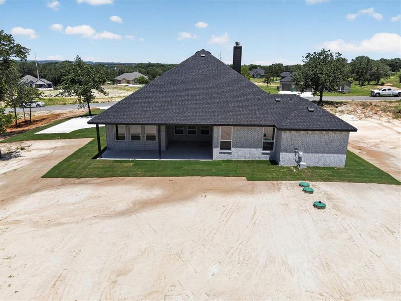 Rear exterior featuring light grey brick, a dark shingle roof, and a covered concrete patio Rear exterior featuring light grey brick, a dark shingle roof, and a covered concrete patio