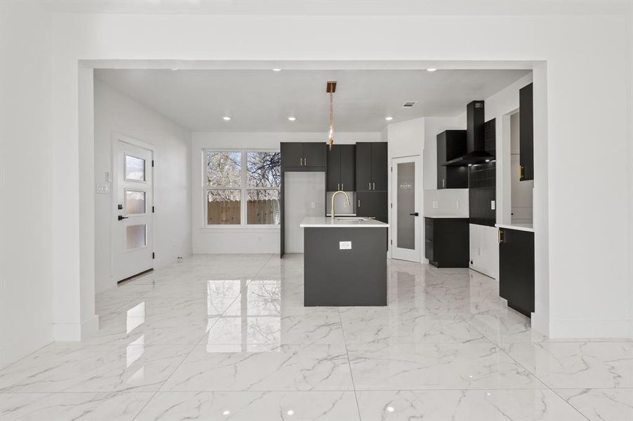 Kitchen with sink, a center island with sink, wall chimney range hood, and hanging light fixtures