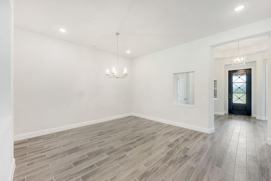 Empty dining room with chandelier, wood-look tile floors, and view of front entry door