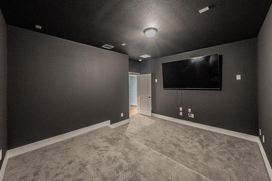 Dedicated media room featuring dark walls and ceiling, wall-mounted television, recessed lighting, and carpeted flooring