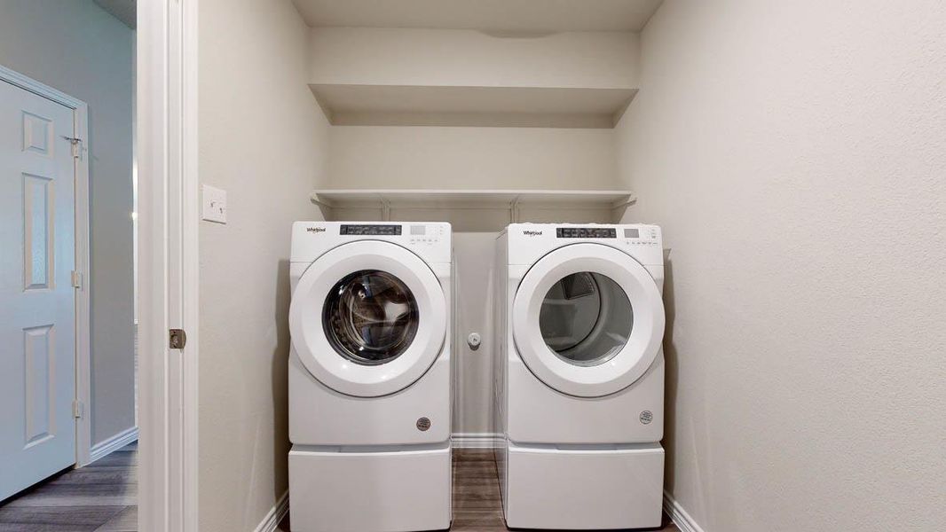 Dedicated laundry area featuring a front-loading washer and dryer, integrated pedestals, and overhead shelving