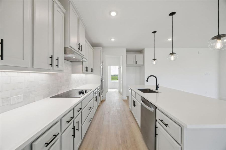 Kitchen featuring white cabinets, a center island with sink, hanging light fixtures, light wood finished floors, and stainless steel dishwasher Kitchen featuring white cabinets, a center island with sink, hanging light fixtures, light wood finished floors, and stainless steel dishwasher
