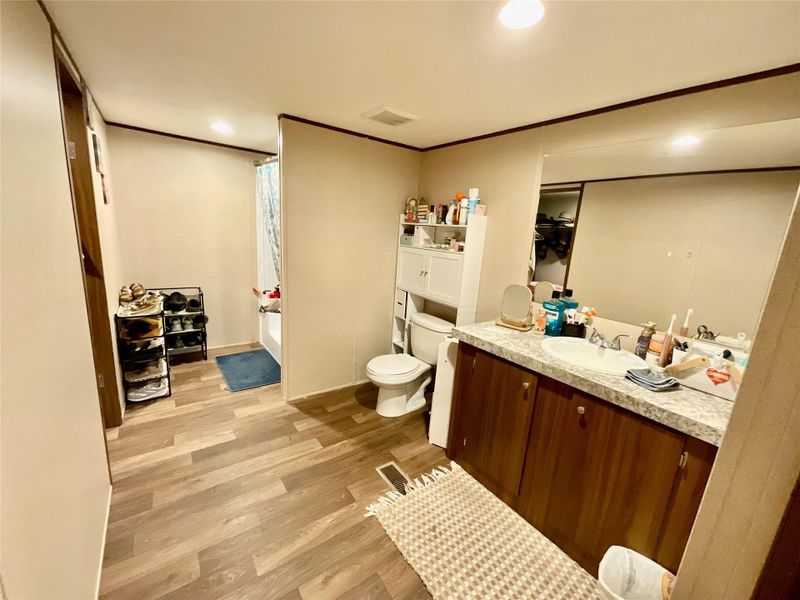 Bathroom featuring wood-finish flooring, a vanity with wood-finish cabinetry, a white basin, a mounted mirror, and a built-in bathtub with shower