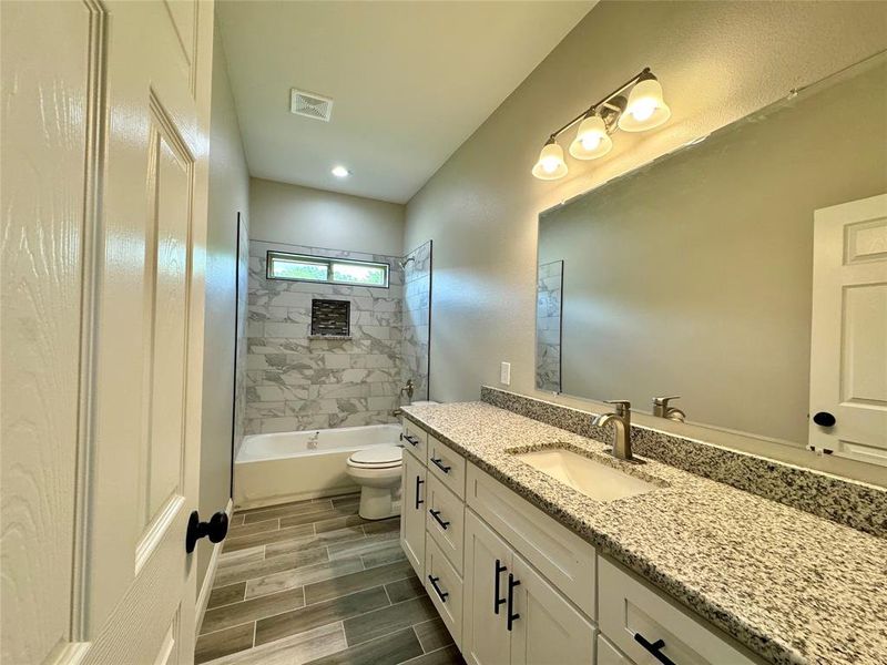 Full bathroom with tile patterned flooring, tiled shower / bath combo, toilet, and vanity