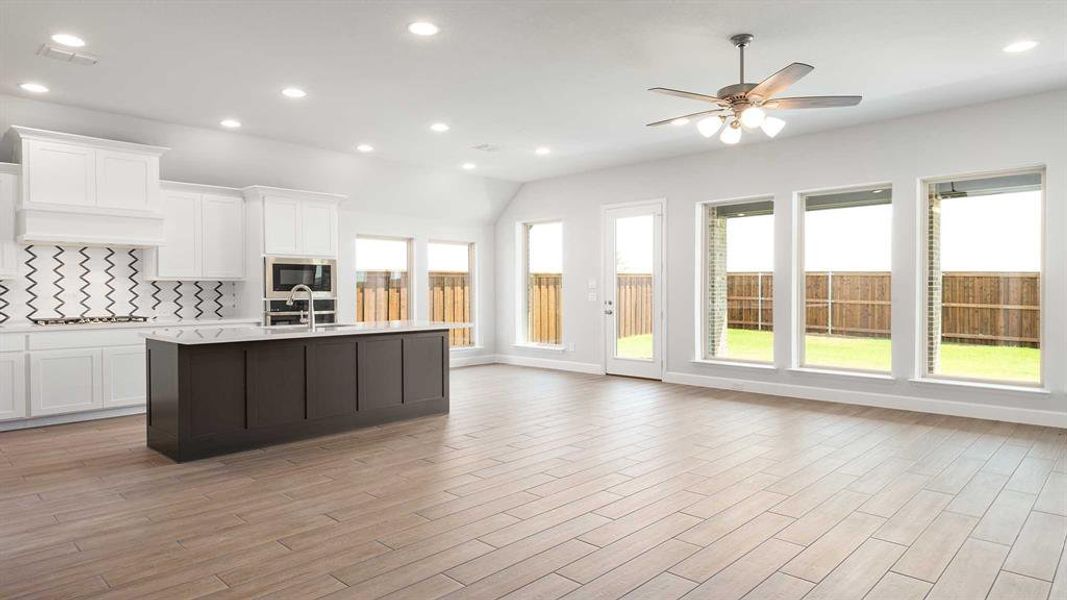 Kitchen featuring light wood-type flooring, white cabinets, ceiling fan, and an island with sink