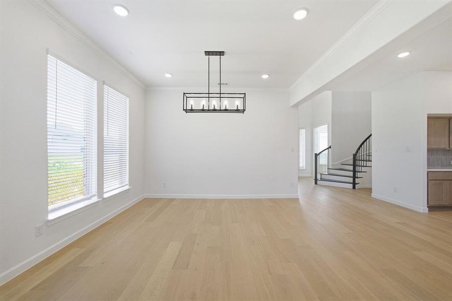 Spacious room featuring light wood-finish flooring, two large windows with blinds, a modern black chandelier, recessed lighting, and crown molding