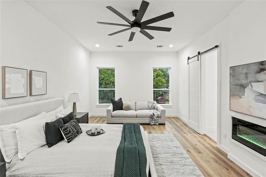 Bedroom with light hardwood / wood-style floors, ceiling fan, and a barn door