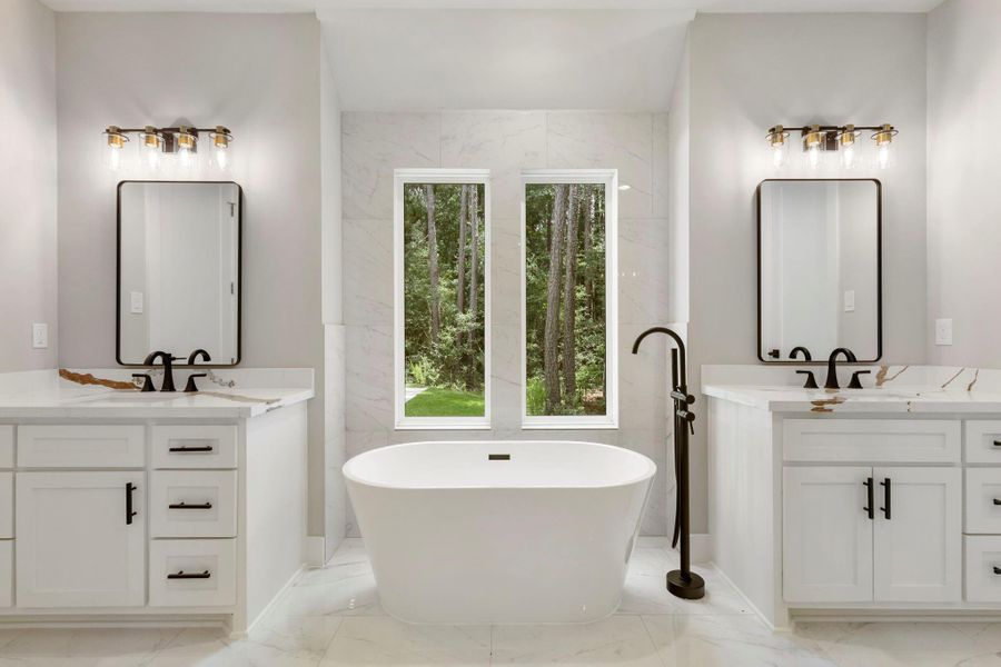 This primary en-suite features a modern, elegant design with a freestanding tub centered between dual vanities. Natural light flows in through a large window, highlighting the sleek fixtures and sleek flooring.