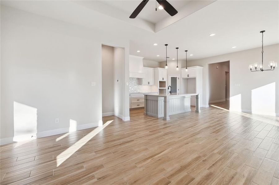 Kitchen with pendant lighting, ceiling fan with notable chandelier, a spacious island, tasteful backsplash, and white cabinetry