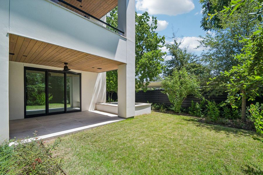 A covered patio with wood-paneled ceilings overlooks a lush, grassy yard. A covered patio with wood-paneled ceilings overlooks a lush, grassy yard.