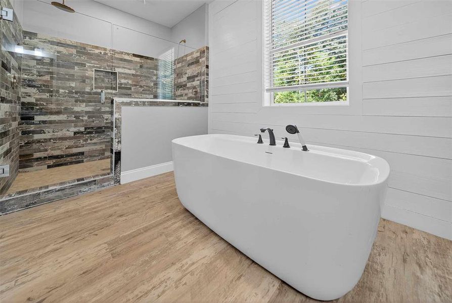 Full bath featuring a freestanding bath, a walk in shower, light wood finished floors, and wood walls