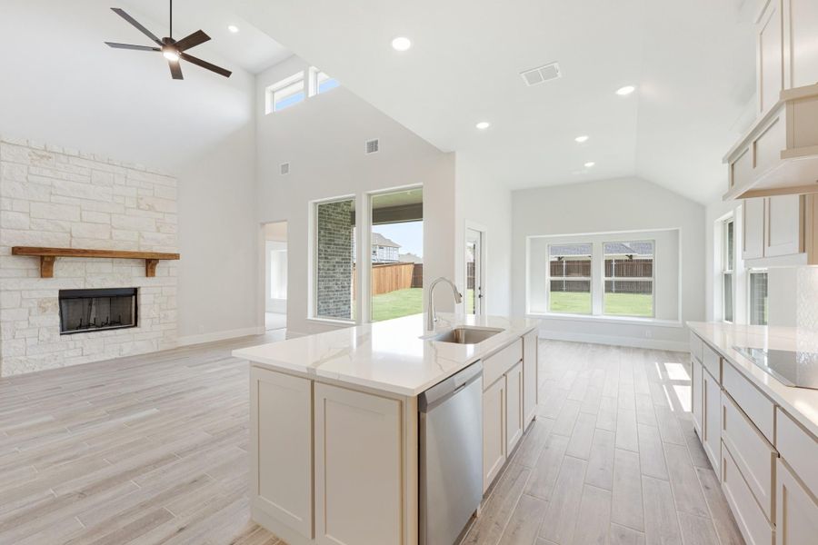 Open kitchen with island, quartz countertops, and vaulted ceiling overlooking living room with stone fireplace