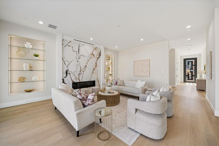 The expansive living room captivates with a statement fireplace framed by built-in, illuminated glass shelving — perfect for display.