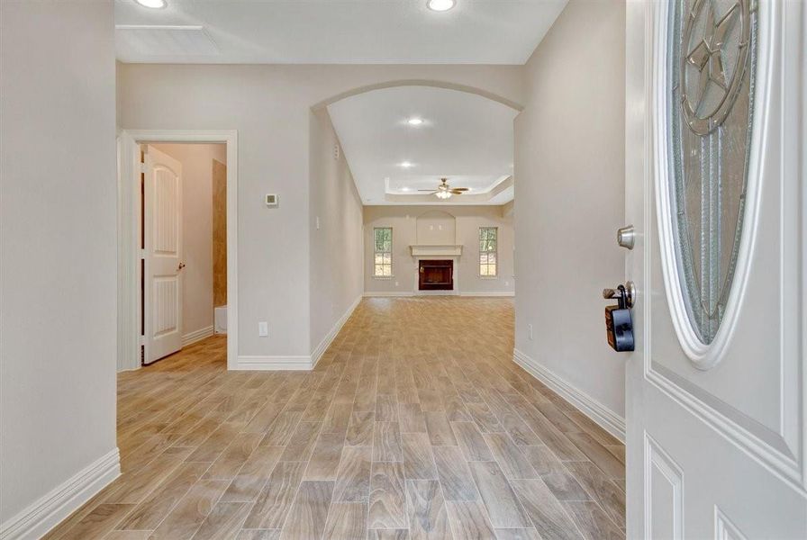 This inviting entryway features wood-look flooring and neutral walls, leading into a spacious living area with a fireplace and natural light from large windows. The arched ceiling detail adds elegance to the space. This inviting entryway features wood-look flooring and neutral walls, leading into a spacious living area with a fireplace and natural light from large windows. The arched ceiling detail adds elegance to the space.