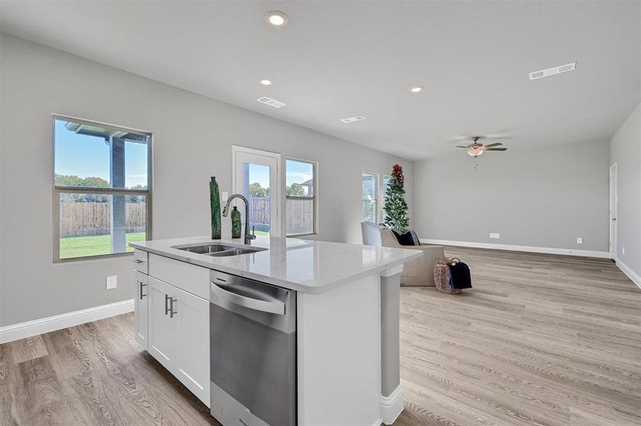 Kitchen featuring sink, stainless steel dishwasher, a center island with sink, white cabinets, and light wood-type flooring