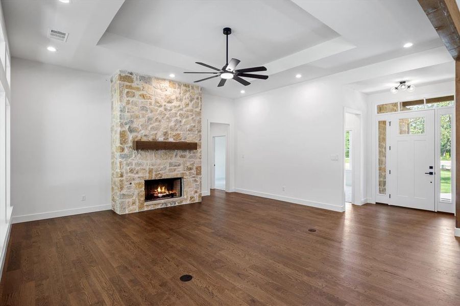 Unfurnished living room with a tray ceiling, dark wood-style flooring, a stone fireplace, ceiling fan, and recessed lighting Unfurnished living room with a tray ceiling, dark wood-style flooring, a stone fireplace, ceiling fan, and recessed lighting
