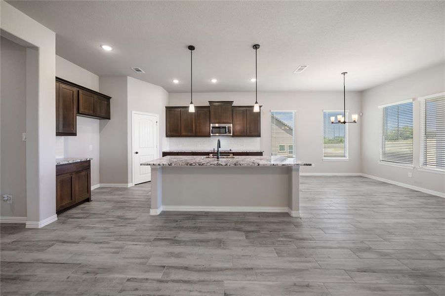 Kitchen with dark brown cabinets, light stone counters, decorative light fixtures, light wood-style floors, and recessed lighting Kitchen with dark brown cabinets, light stone counters, decorative light fixtures, light wood-style floors, and recessed lighting