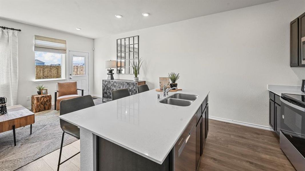 Kitchen with appliances with stainless steel finishes, a breakfast bar area, dark wood-style floors, a kitchen island with sink, and recessed lighting