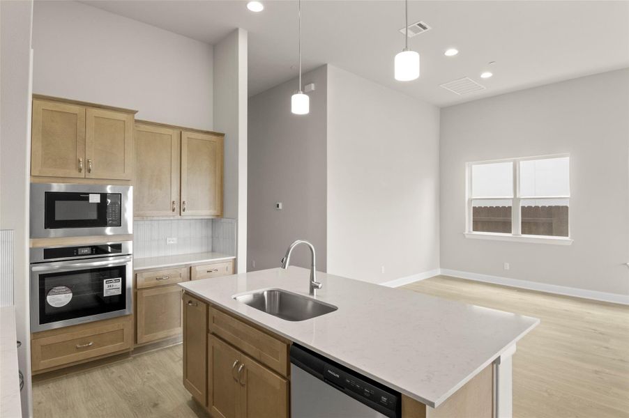 Kitchen featuring a sink, appliances with stainless steel finishes, light wood-type flooring, decorative backsplash, and decorative light fixtures