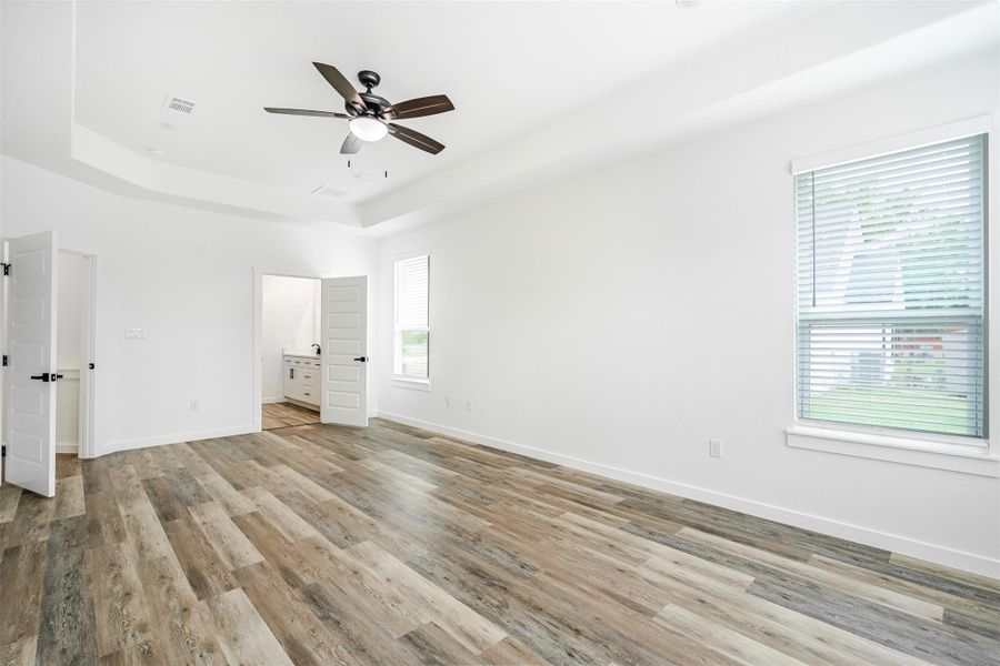A spacious primary bedroom featuring a tray ceiling and light wood-look flooring. A spacious primary bedroom featuring a tray ceiling and light wood-look flooring.