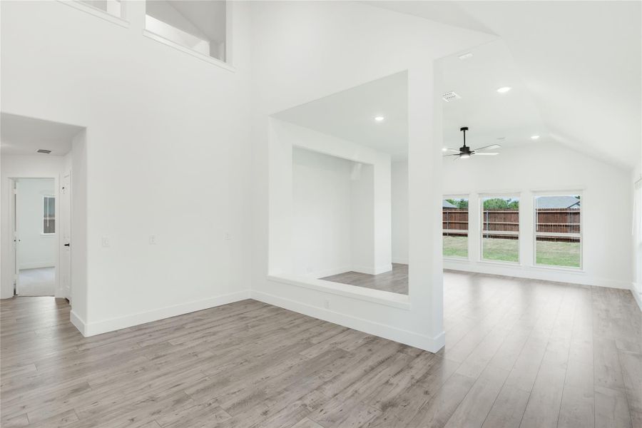 Open living area with vaulted ceiling, ceiling fan, hardwood floors, and large backyard-facing windows Open living area with vaulted ceiling, ceiling fan, hardwood floors, and large backyard-facing windows