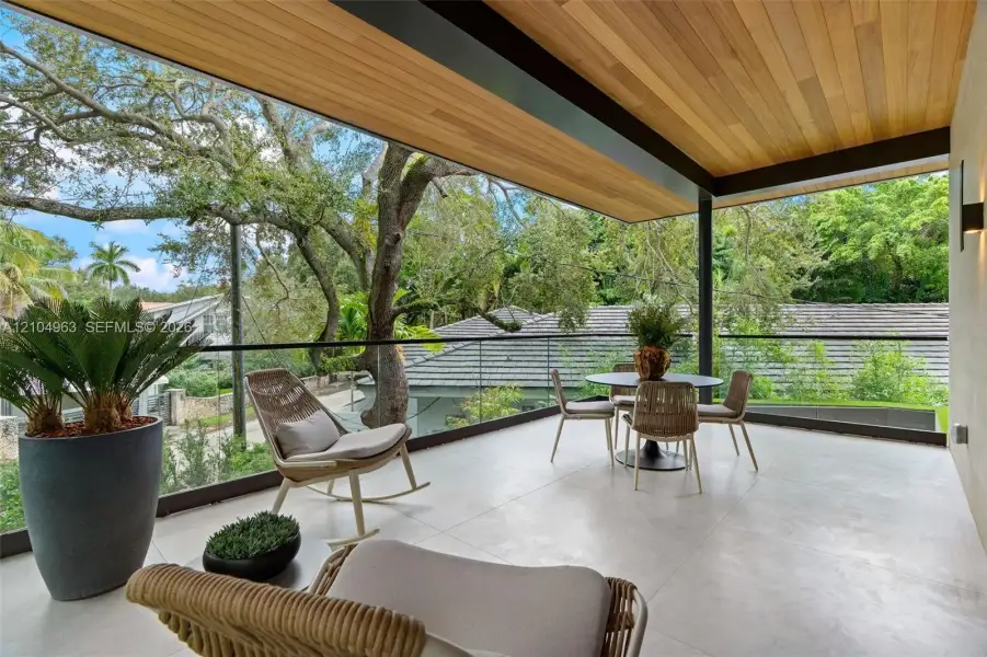 Covered balcony featuring wood-plank ceiling finish, large-format tile flooring, and a frameless glass railing system
